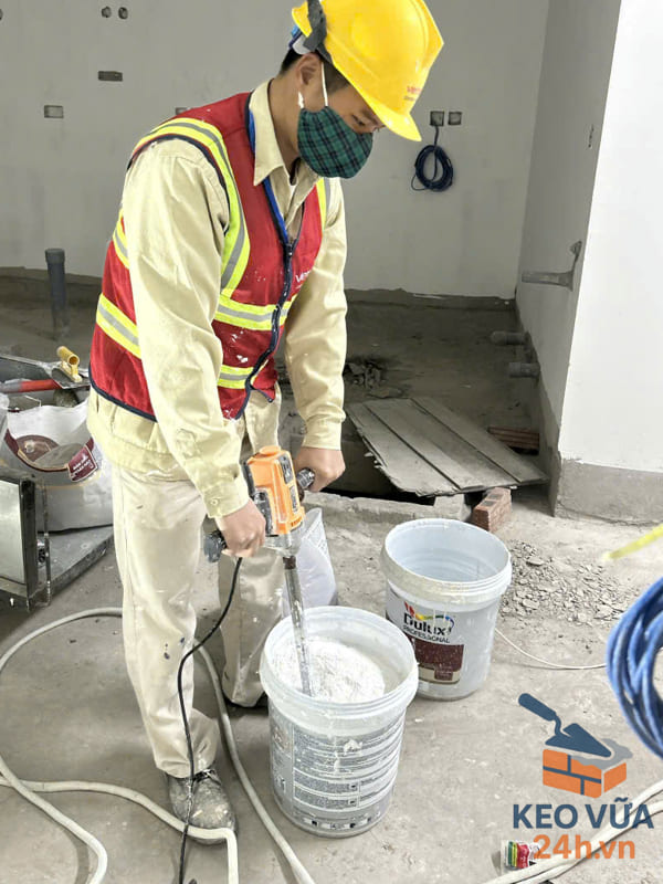 Công nhân trộn bột bả skimcoat với nước và khuấy đều bằng máy.